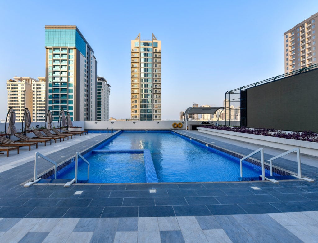 A House Me Bahrain company provides a swimming pool in Bahrain, with lounge chairs and tall buildings surrounding the area.