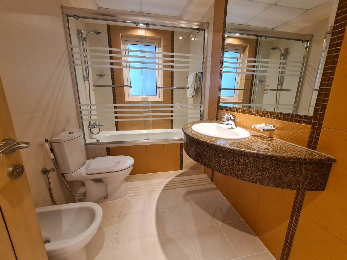 A stunning apartment for sale in the heart of Juffair, featuring two bedrooms and a bathroom with a toilet, sink and mirror.