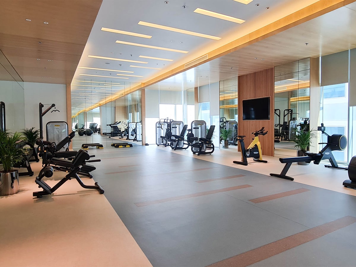 Fully furnished luxury 1BR apartment with a gym room equipped with exercise equipment and mirrors.