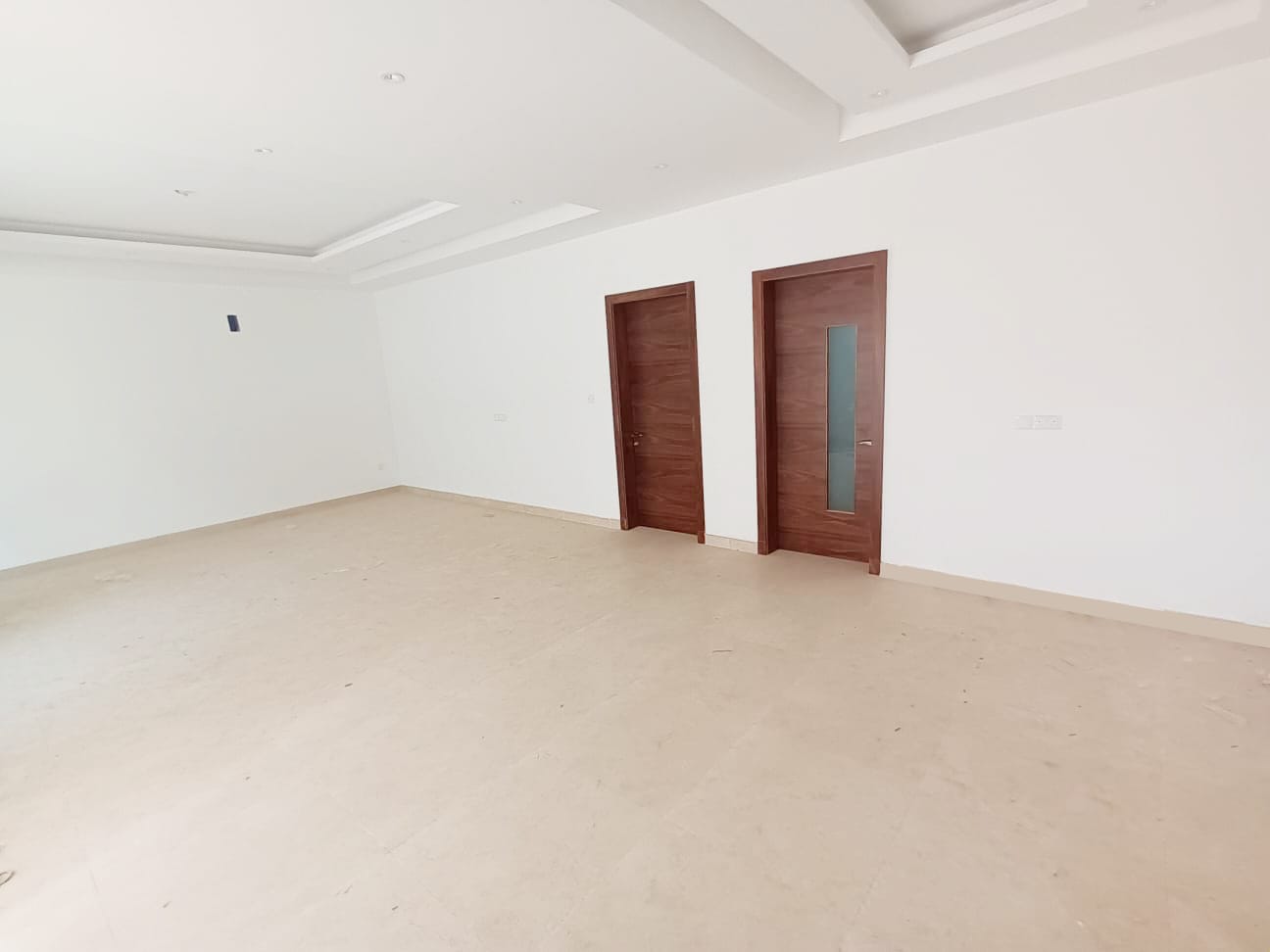 Empty room with wooden doors and white walls in a 4BR Villa for Sale in Bani Jamra.