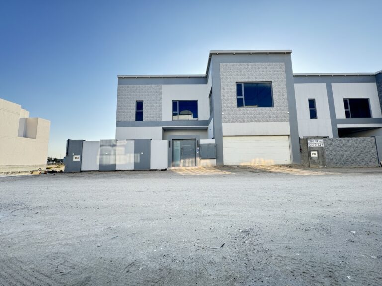 Newly constructed modern villa in Saraya 2 with large front gate and clear blue sky.