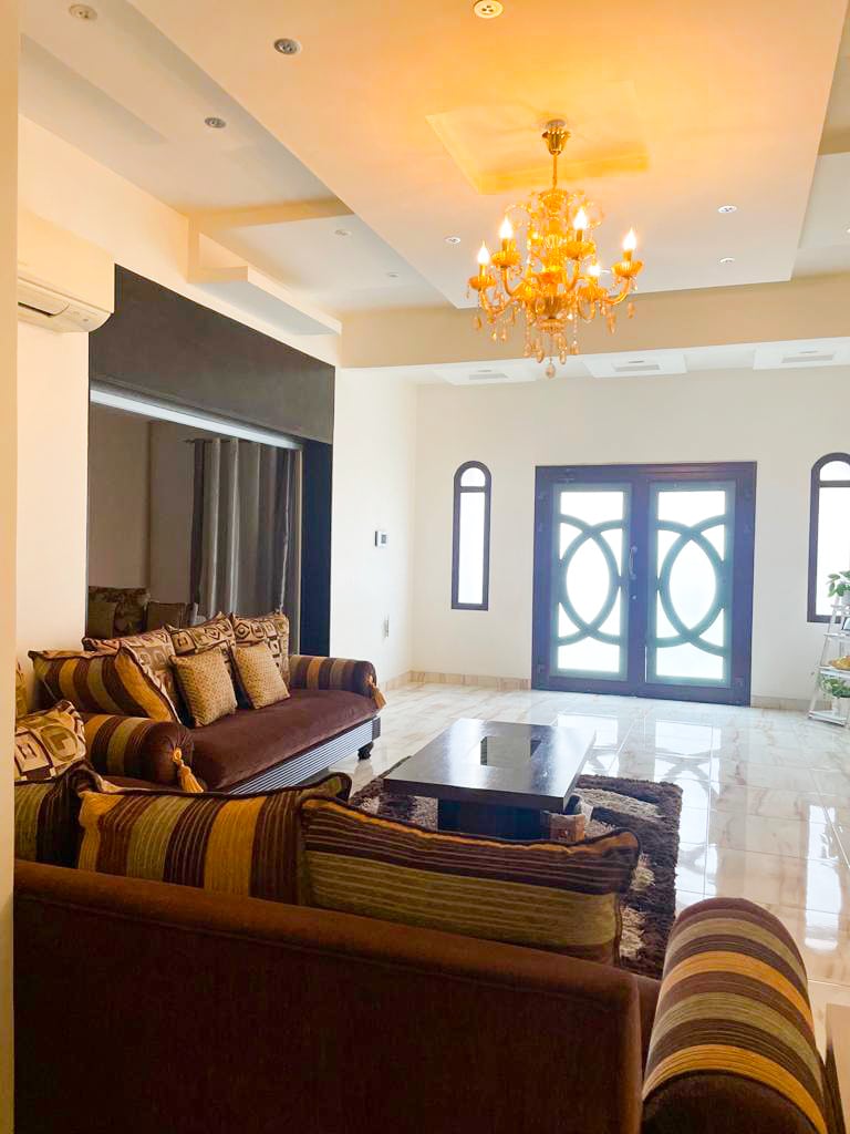 A wonderful living room with couches and a chandelier in a 5BR Villa for Sale in Muharraq with a garden.