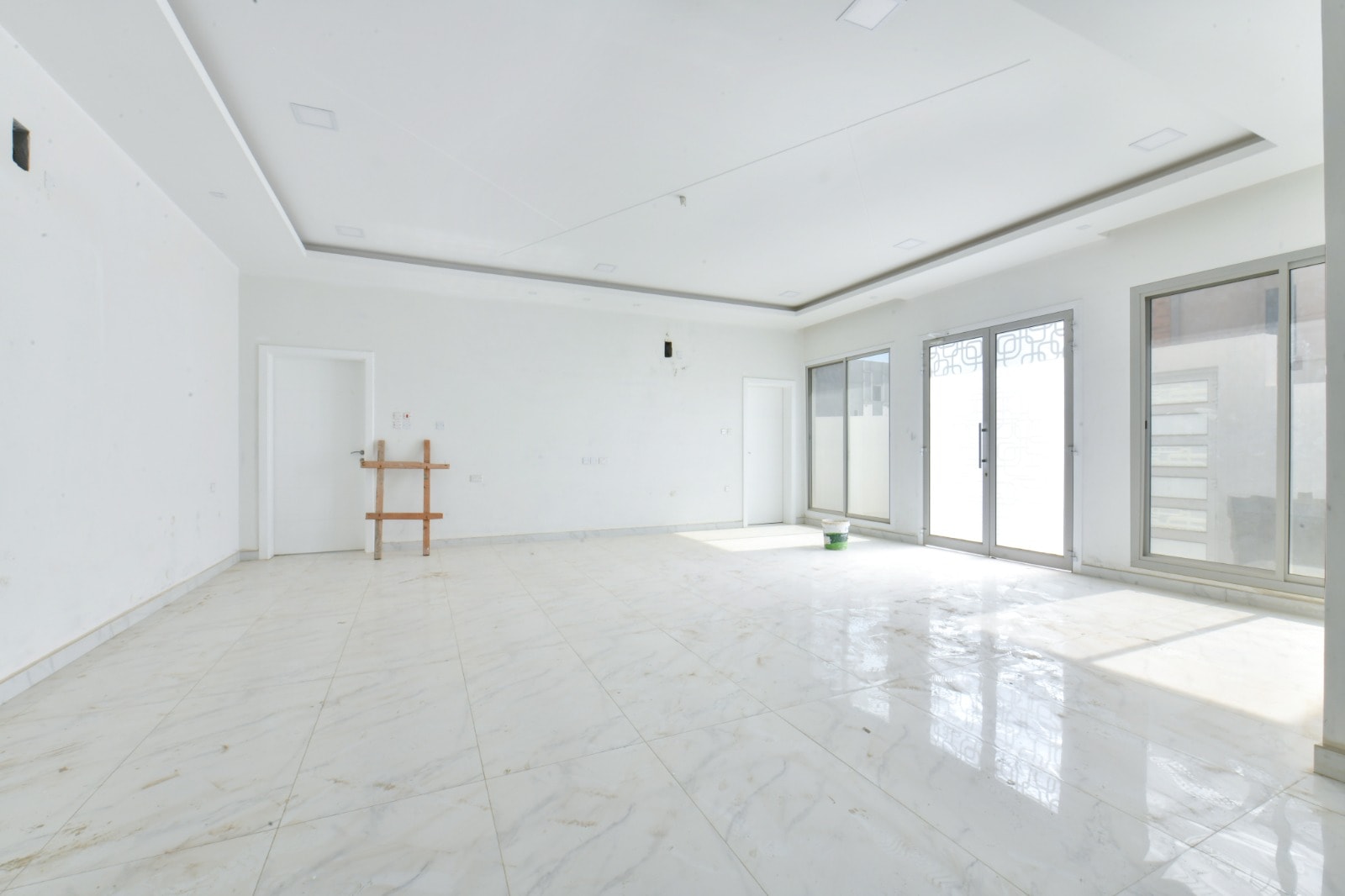 An empty room with white tile floors and sliding glass doors in an amazing villa for sale.