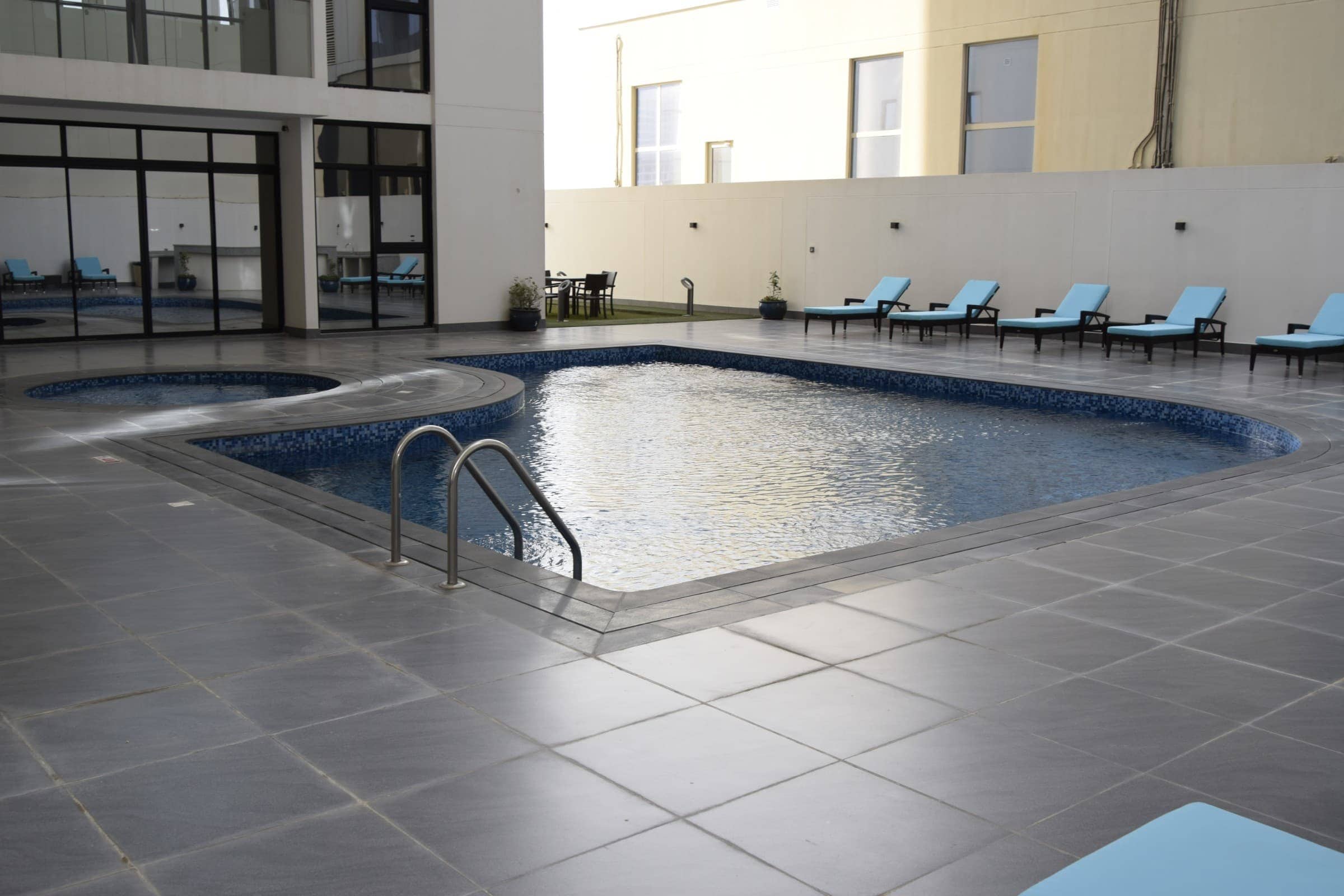 For sale, a fully furnished 1BR unit in a building with a swimming pool and lounge chairs.