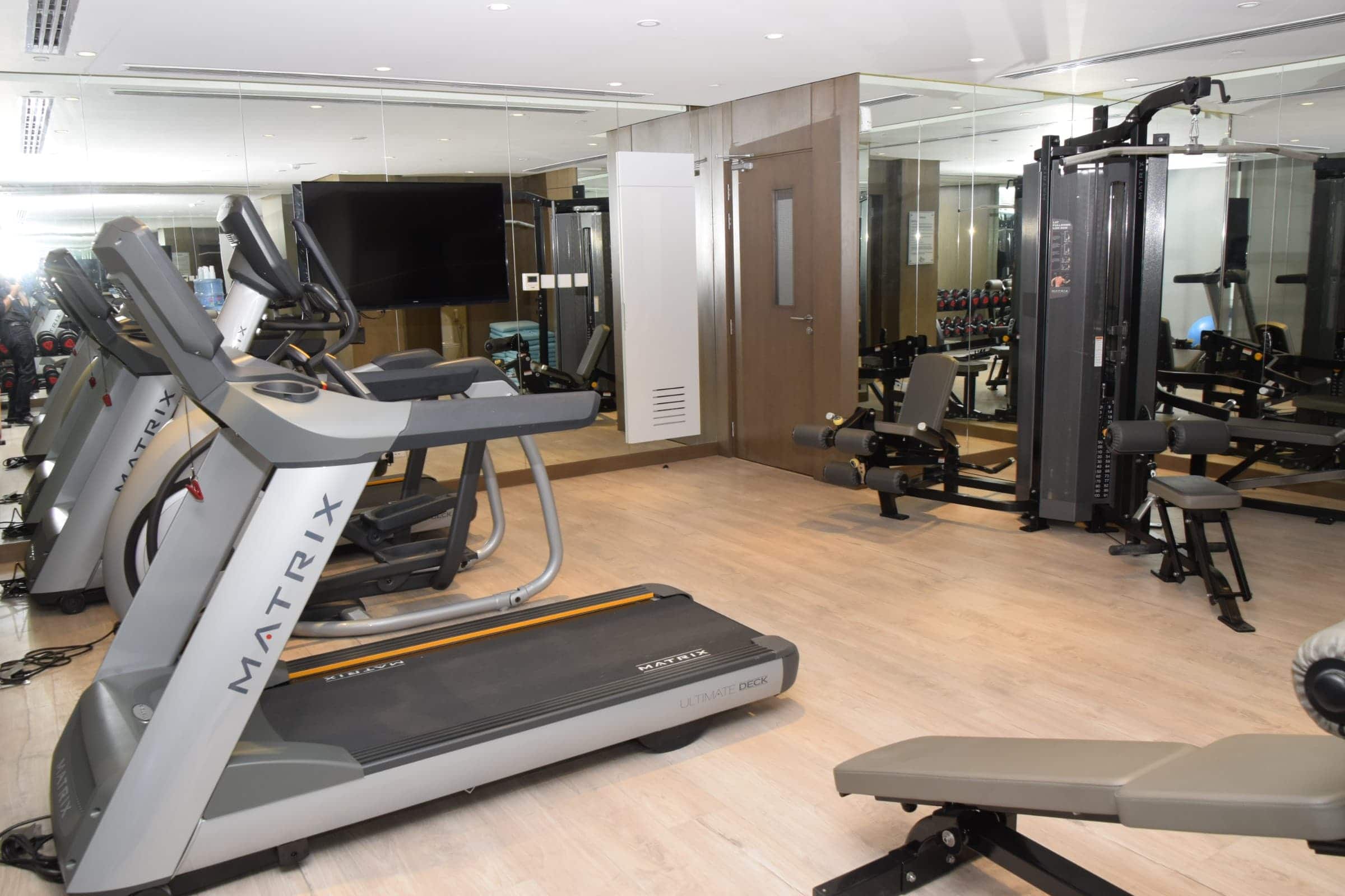 A fully furnished gym room with a treadmill, elliptical, and weights.