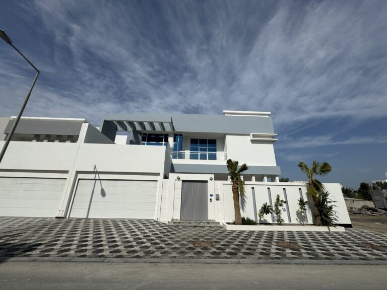 A luxurious villa with a grey door and palm trees for sale in Saar.