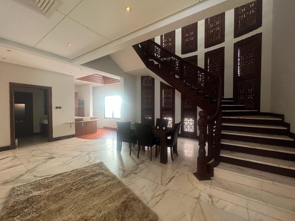 For rent, a luxurious villa in Juffair boasting a spacious living room with an elegant staircase connecting to a captivating dining area.