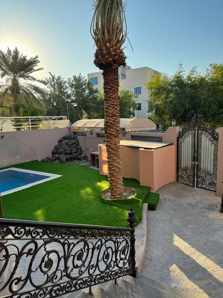 A villa for rent in Juffair with a backyard adorned with artificial grass and a palm tree.