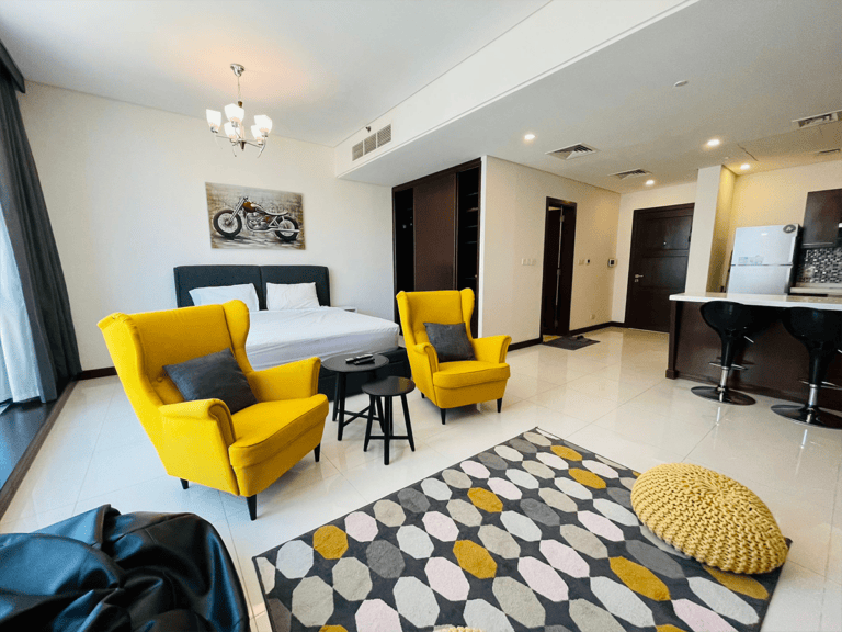 A luxury studio with yellow chairs and a bed in Juffair.