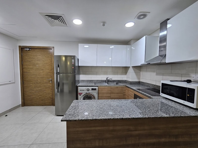 A kitchen with stainless steel appliances and wooden cabinets in a flat for rent in Juffair.