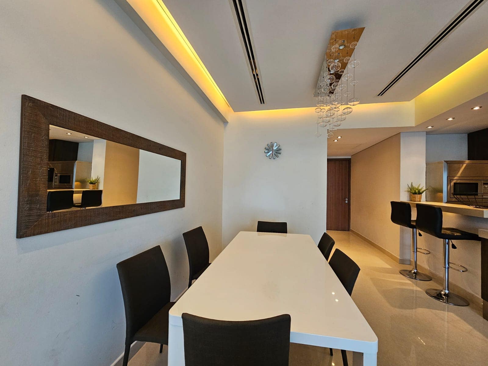 Modern dining room with white table, black chairs, and a kitchen bar area.