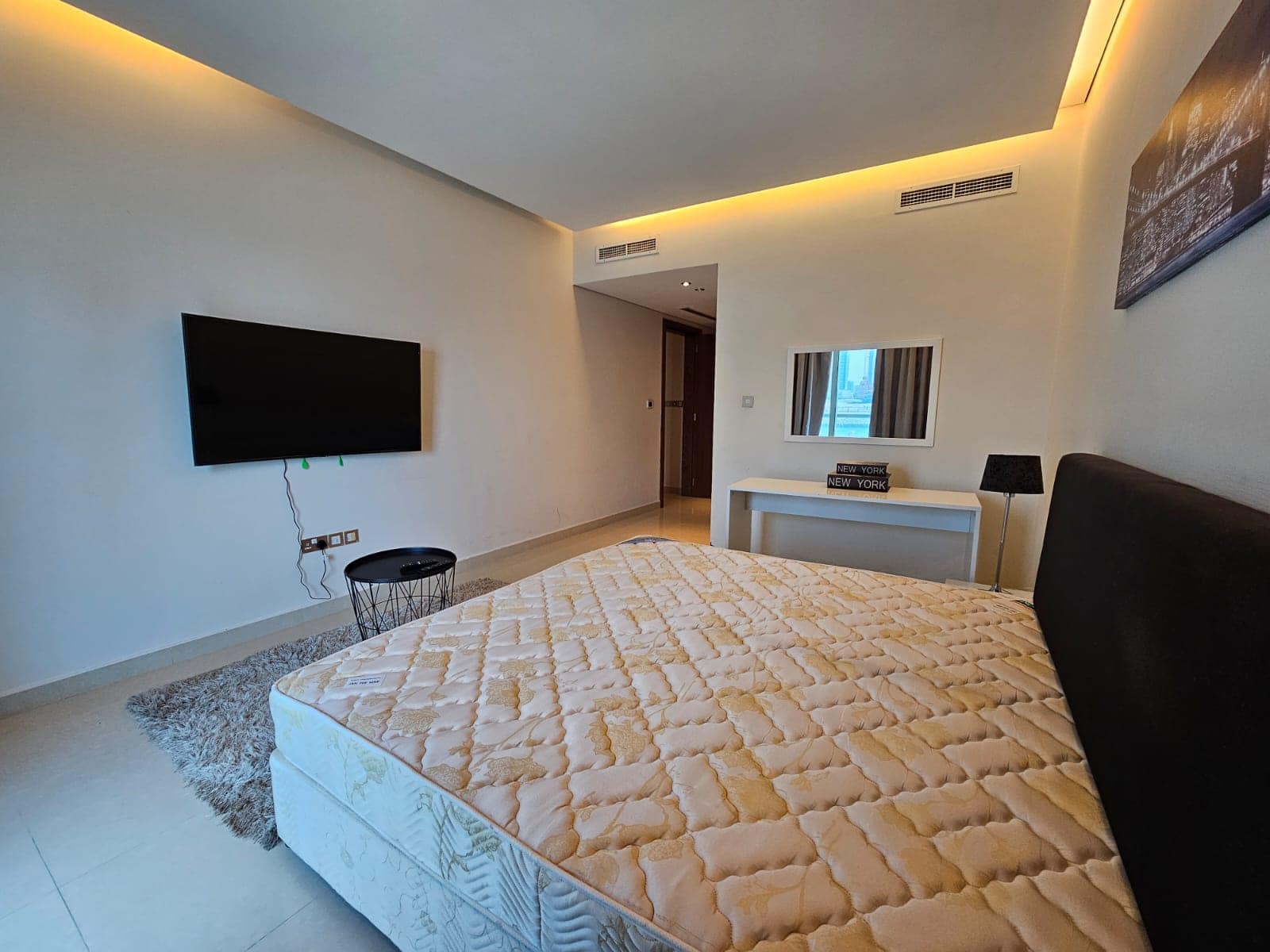 A modern, well-lit bedroom with a large bed, a wall-mounted television, and minimalistic decor.