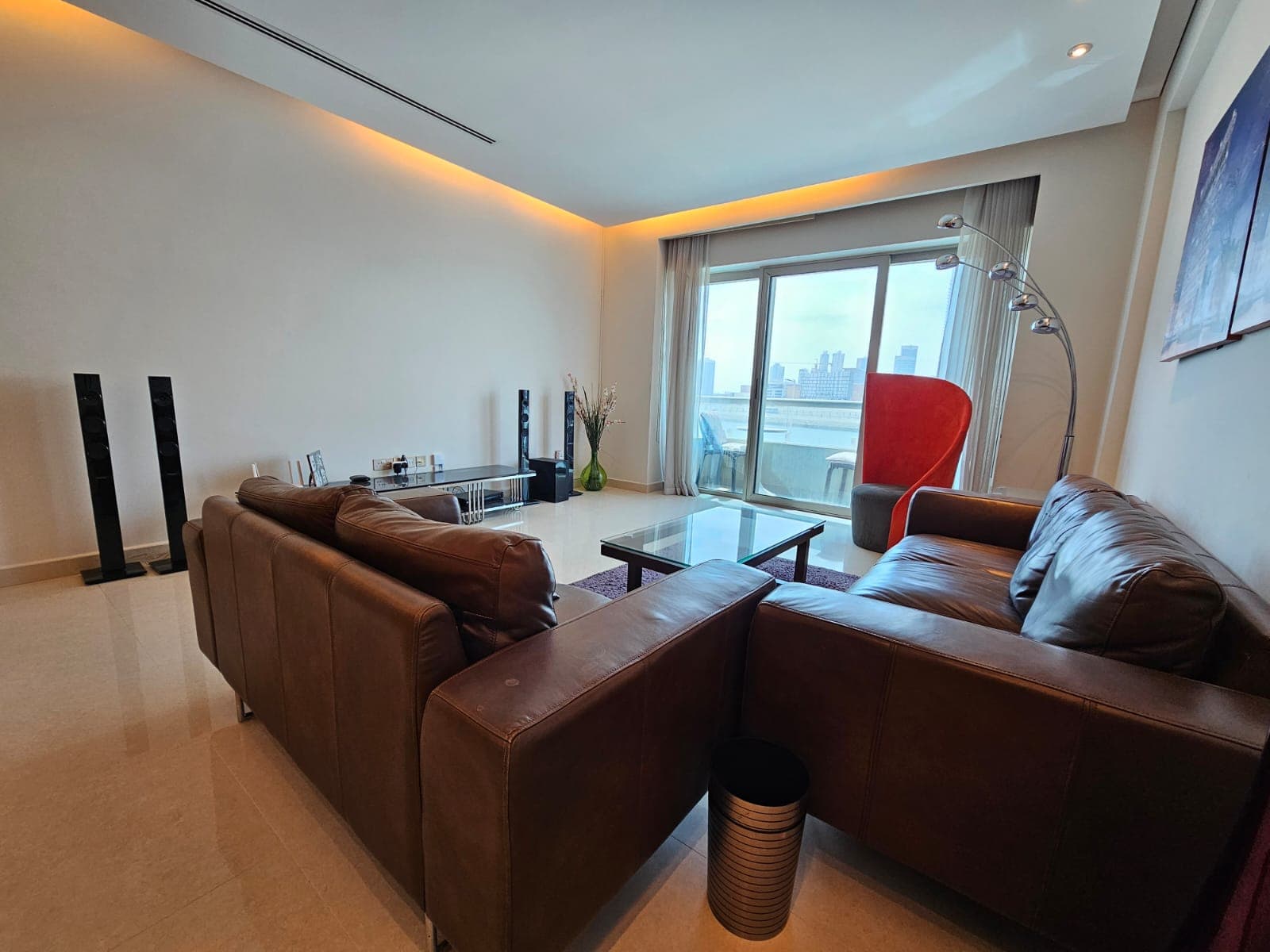 Modern living room with leather sofas, floor lamp, and a view of the city through a large window.