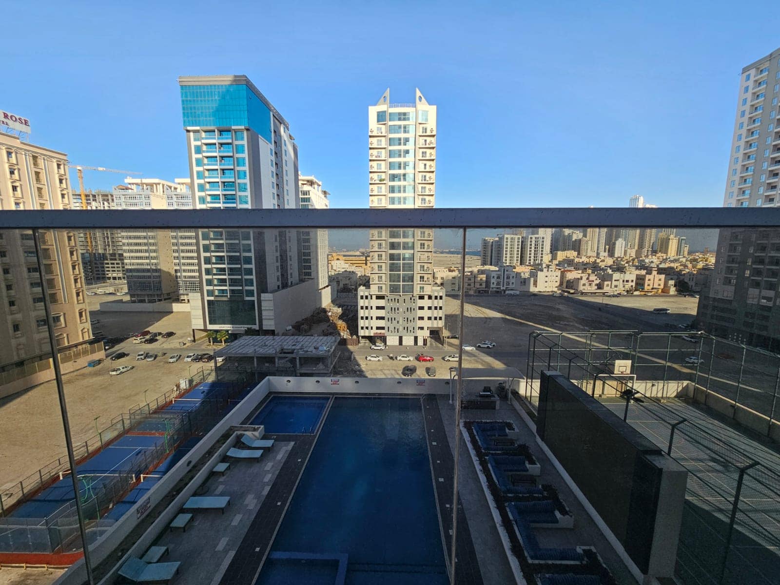 Urban skyline viewed from a luxury apartment balcony overlooking a swimming pool with surrounding high-rise buildings in Juffair under a clear blue sky.