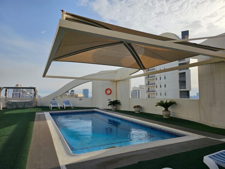Rooftop swimming pool with a retractable awning and cityscape view in a fully-furnished two-bedroom apartment in Juffair.