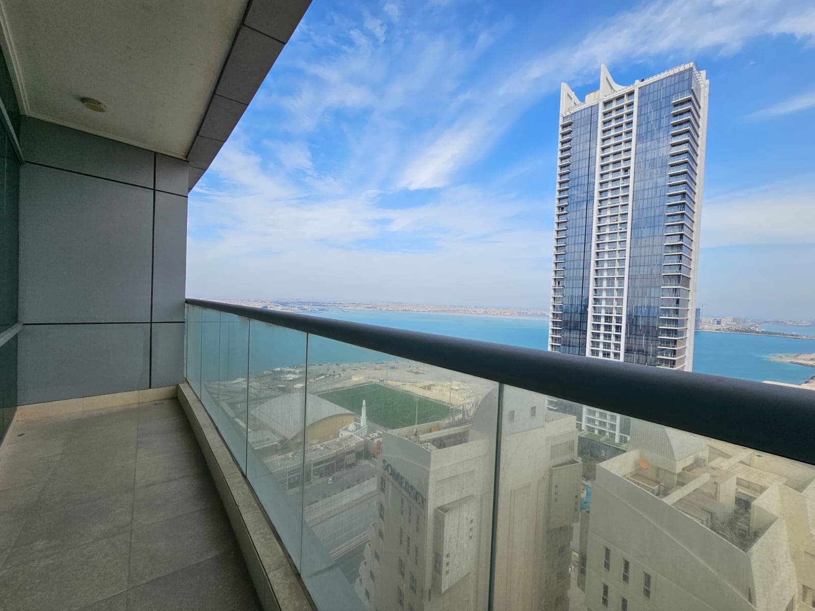 Balcony view of a cityscape with a skyscraper and water body in the distance from a Juffair apartment for rent.