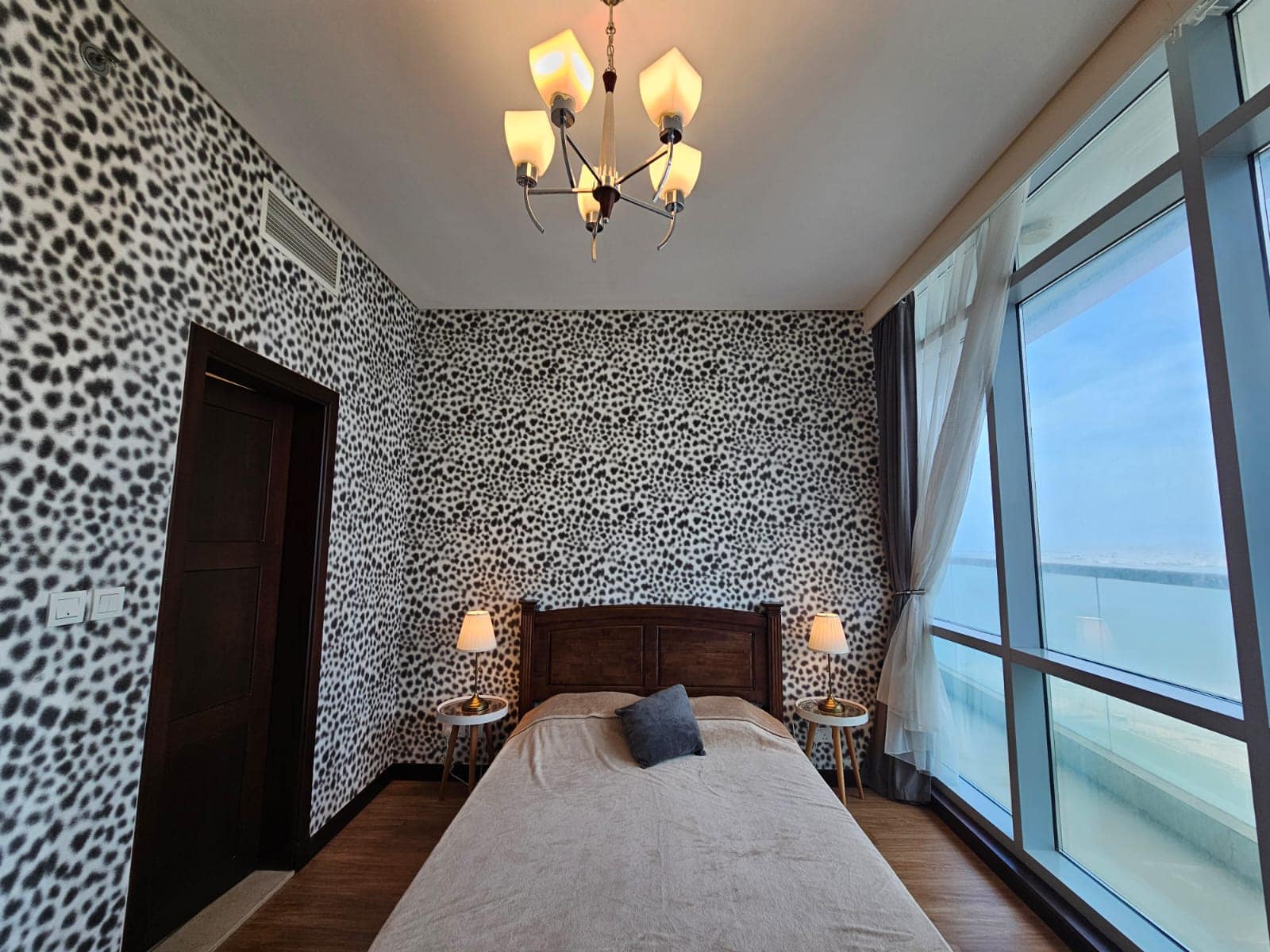 An apartment in Juffair with a bedroom featuring leopard print wallpaper, a large bed, two bedside tables with lamps, and a window offering an ocean view.