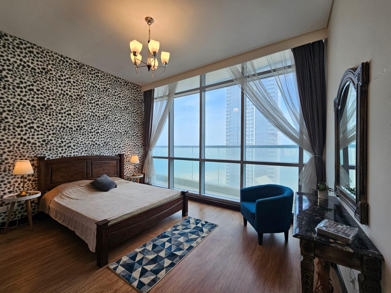 Modern apartment bedroom for rent in Juffair with animal print wallpaper, wooden furniture, and a floor-to-ceiling window offering a city view.