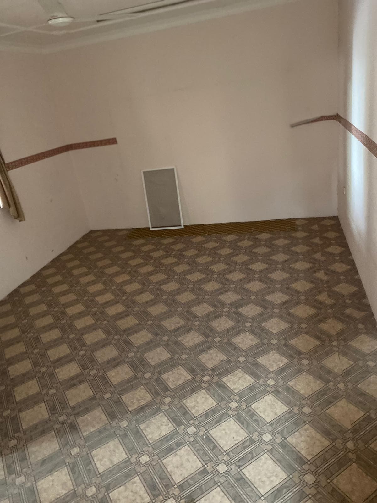 An empty room with tiled floors and a window in a villa for sale in Isa Town.