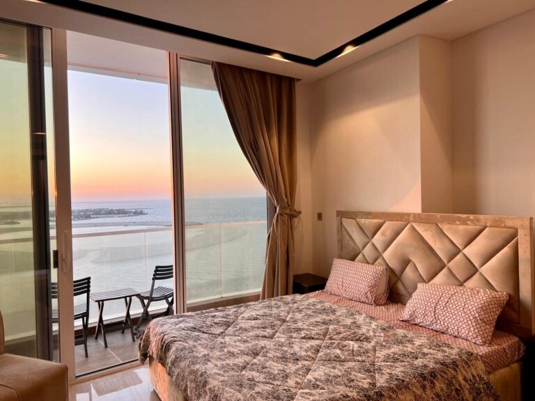 غرفة نوم بها سرير كبير وإطلالة على المحيط عند غروب الشمس.