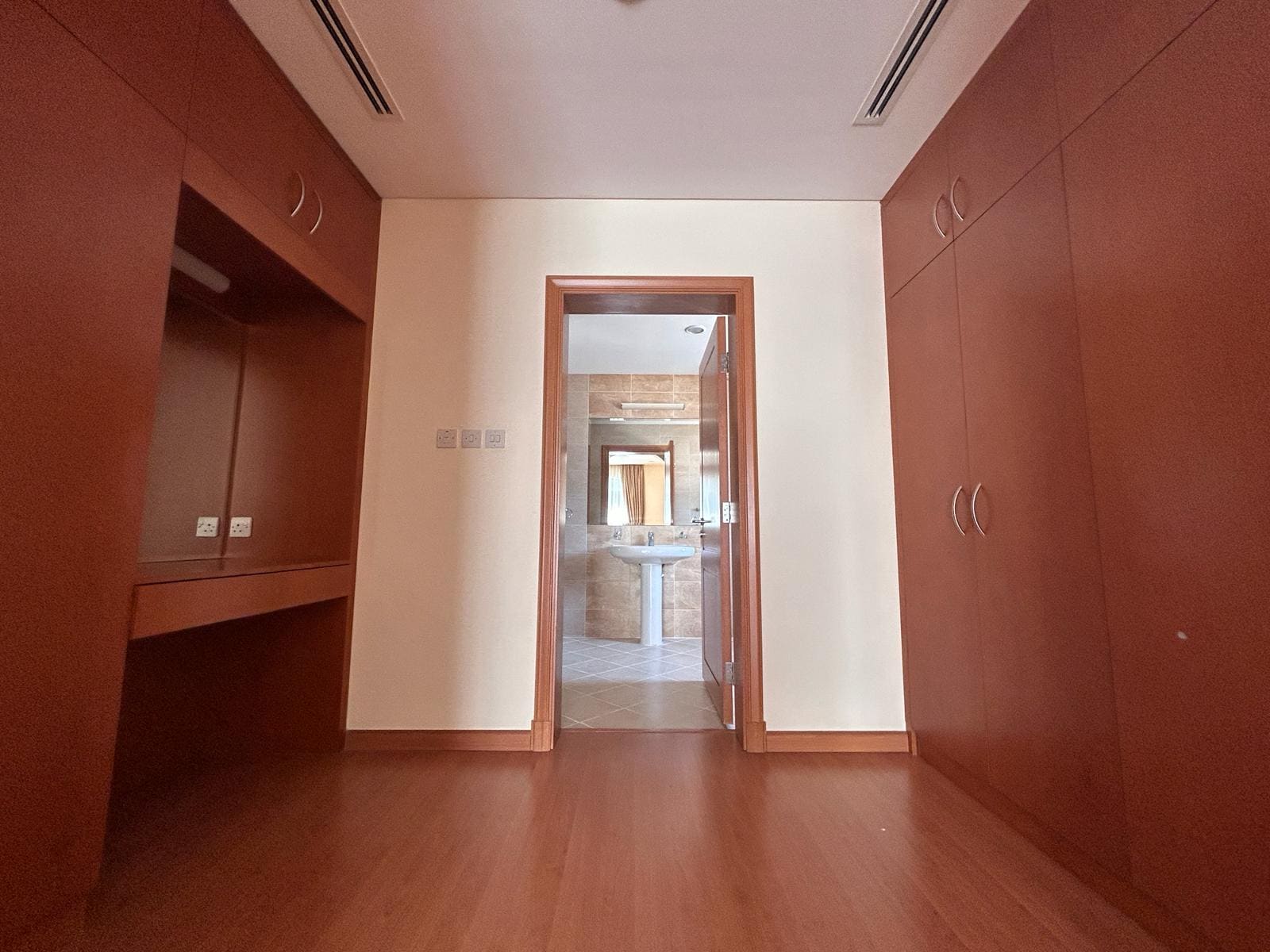 An empty room with wooden cabinetry and an open door leading to an adjoining room in a Villa for Rent in Compound Hamala.