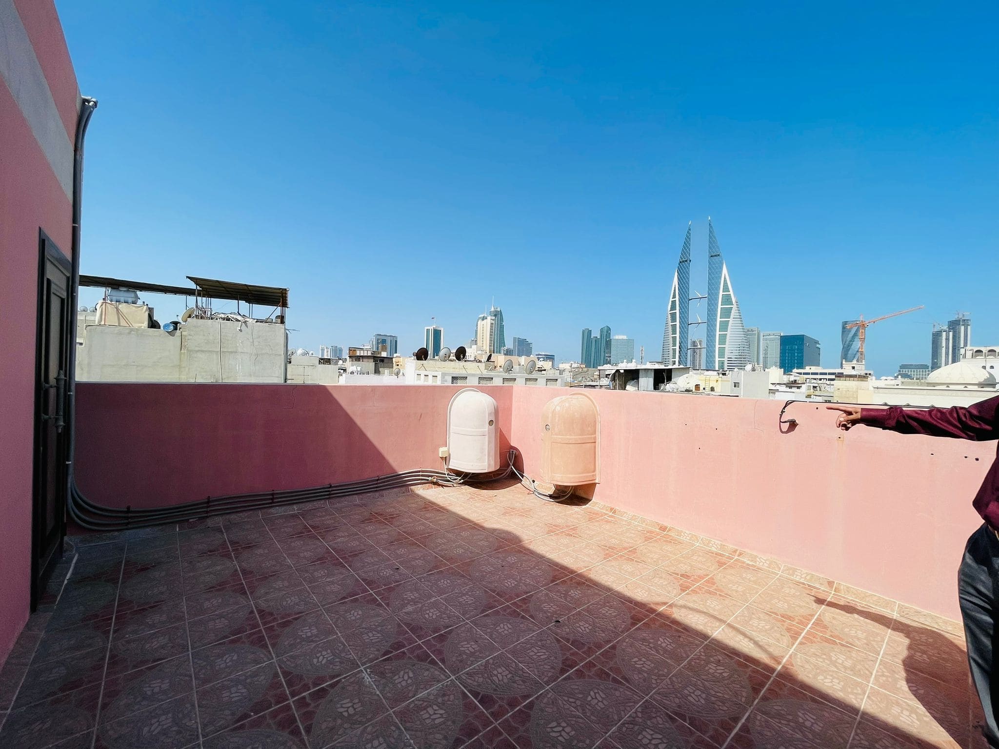 A semi-furnished villa in Ras Rumman offers a rooftop view of a city skyline with distinctive skyscrapers, under a clear blue sky.