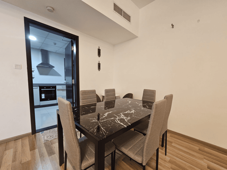 Modern dining area in an elegant apartment with a marble-patterned table and six chairs, adjacent to an open kitchen in the Juffair area available for rent.