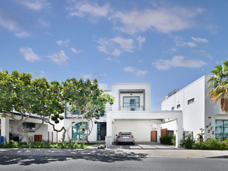 Modern white 5BR villa for rent with a car parked in the driveway under a clear blue sky on Tala Island.