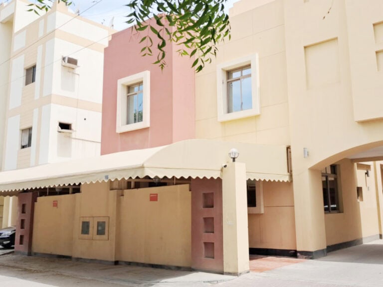 Urban street view showing a pink and a beige Family 3BR Villa with architectural details and a covered sidewalk in the Jid Ali Area.
