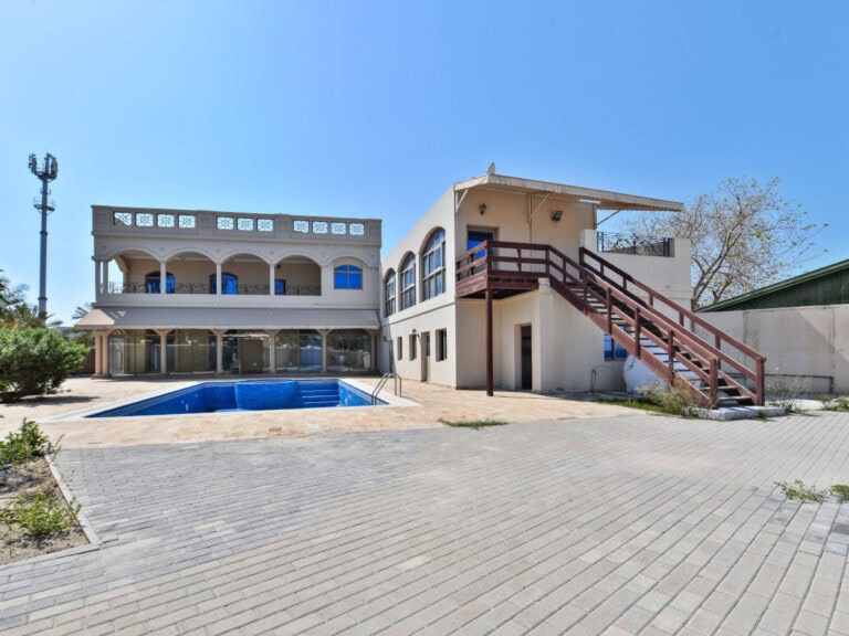 A large two-story 6BR Villa with a blue swimming pool in the courtyard, surrounded by paving and a clear sky above, now available for sale.