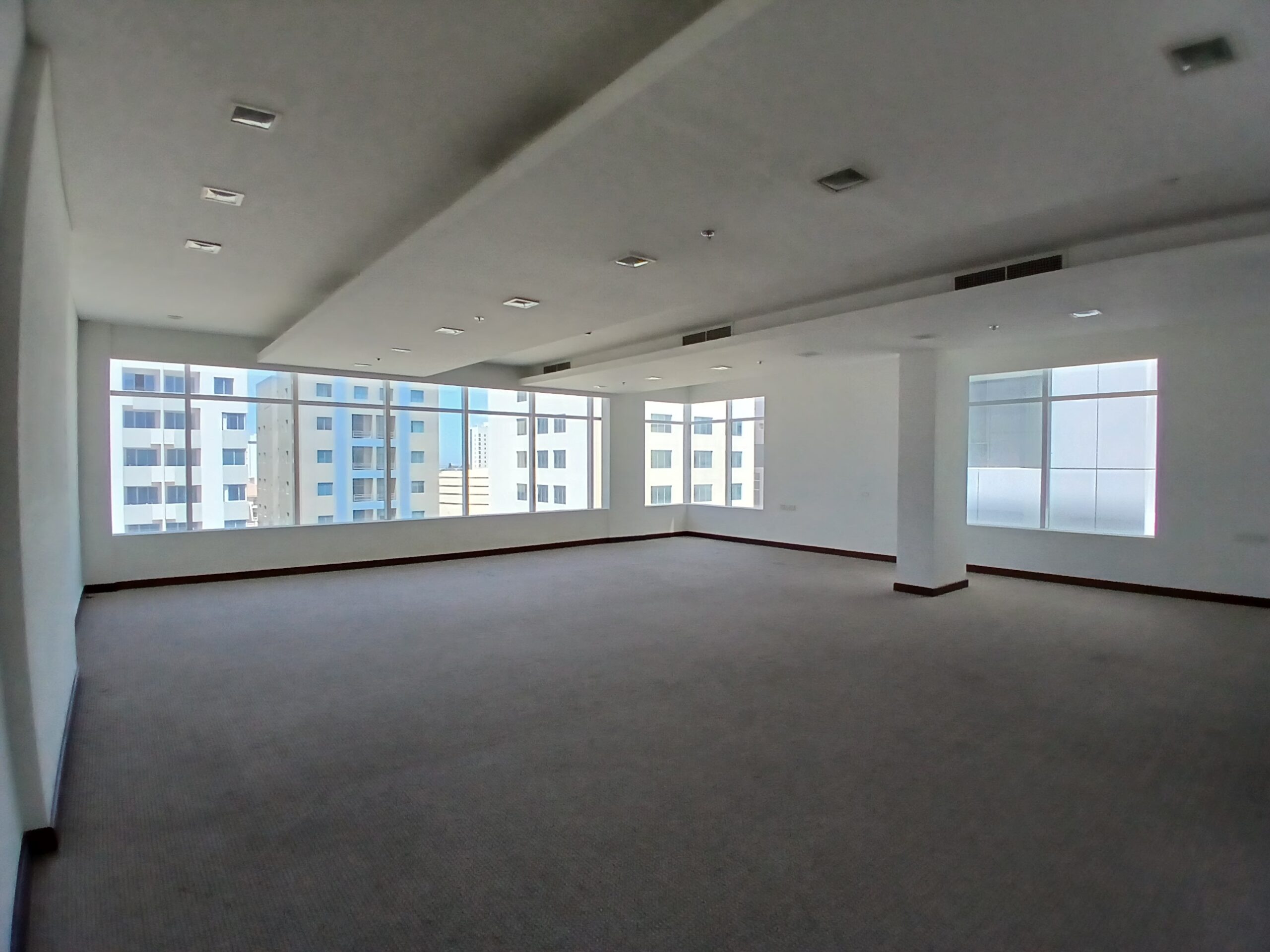 Empty fitted office space with carpeted floors, white walls, and large windows letting in natural light.