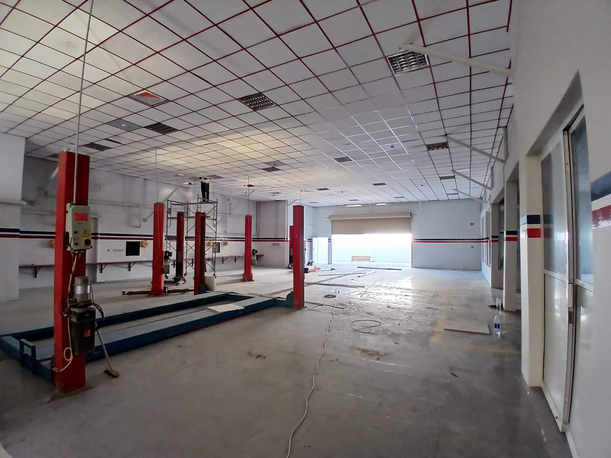 Interior of an empty garage with scattered red hydraulic car lifts, dangling ceiling tiles, and a white and red checkered floor.