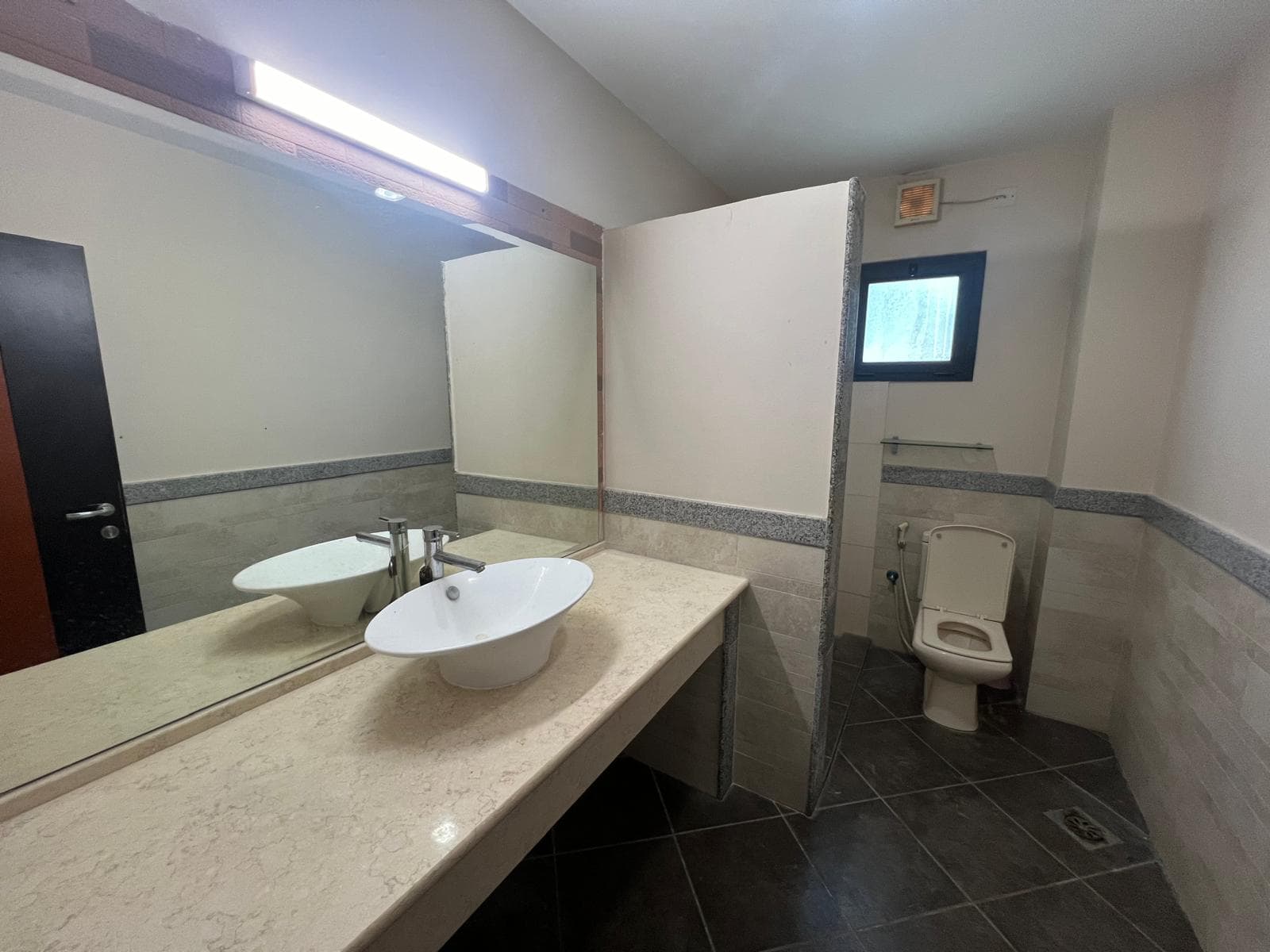 A bathroom interior showing a double sink vanity with mirrors, a toilet, and a partition wall.