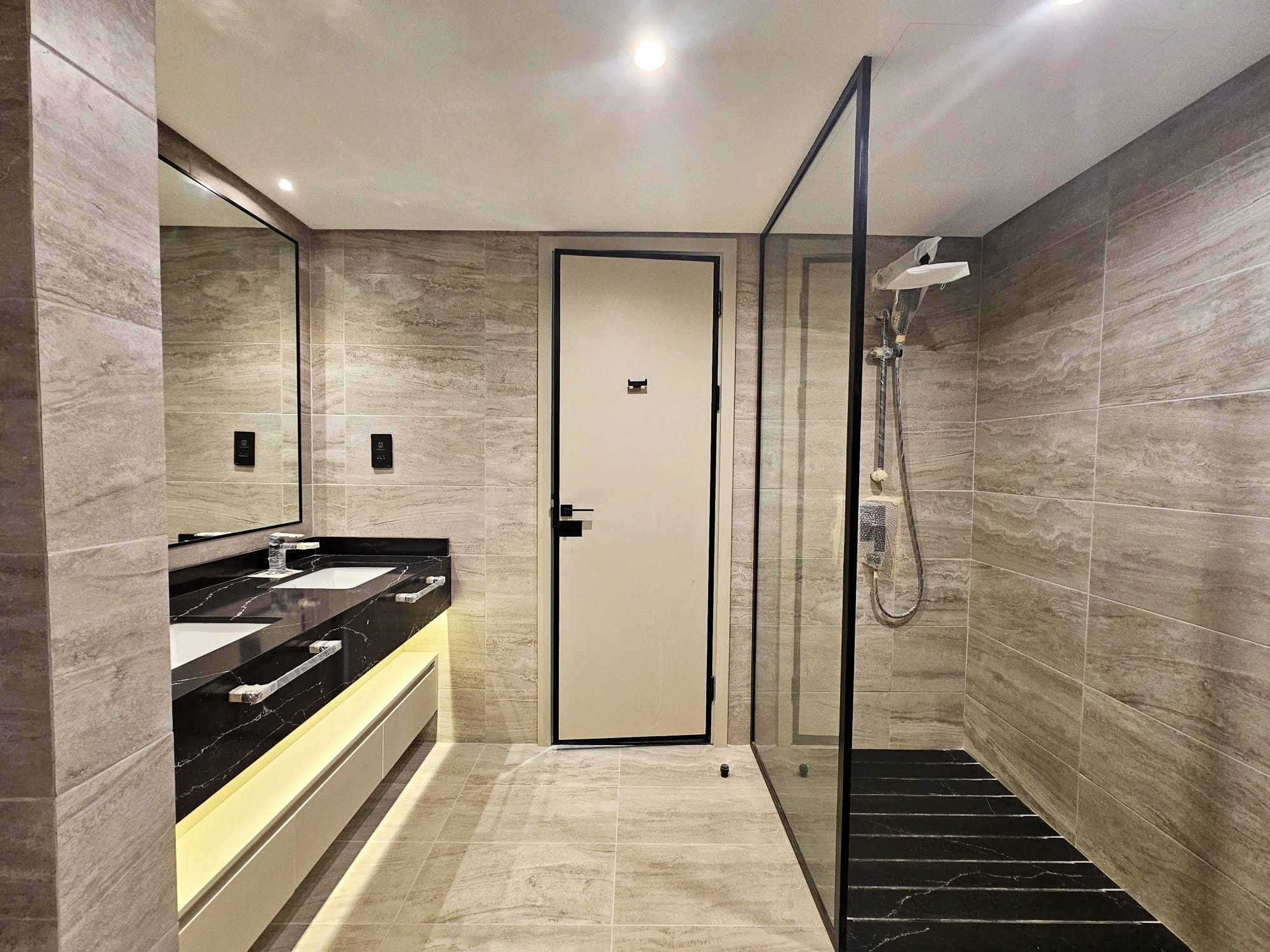 Modern bathroom interior with a walk-in shower, glass partition, wall-mounted sink, and large mirror.