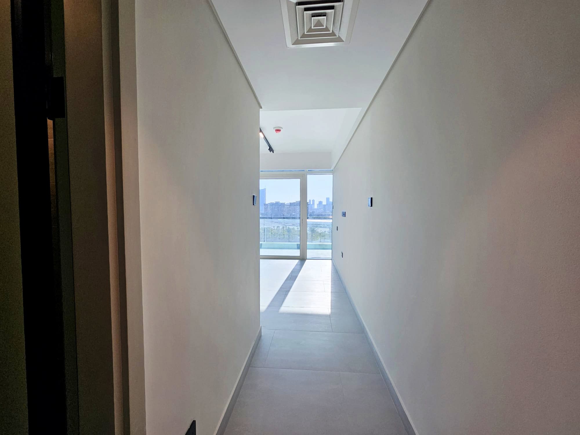 Brightly lit, empty corridor leading towards a window with a view of the skyline. Auto Draft