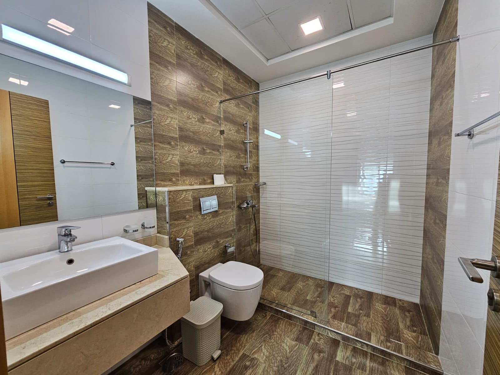 Luxurious modern bathroom interior with glass shower cabin, wooden tiles, and white sanitary ware.