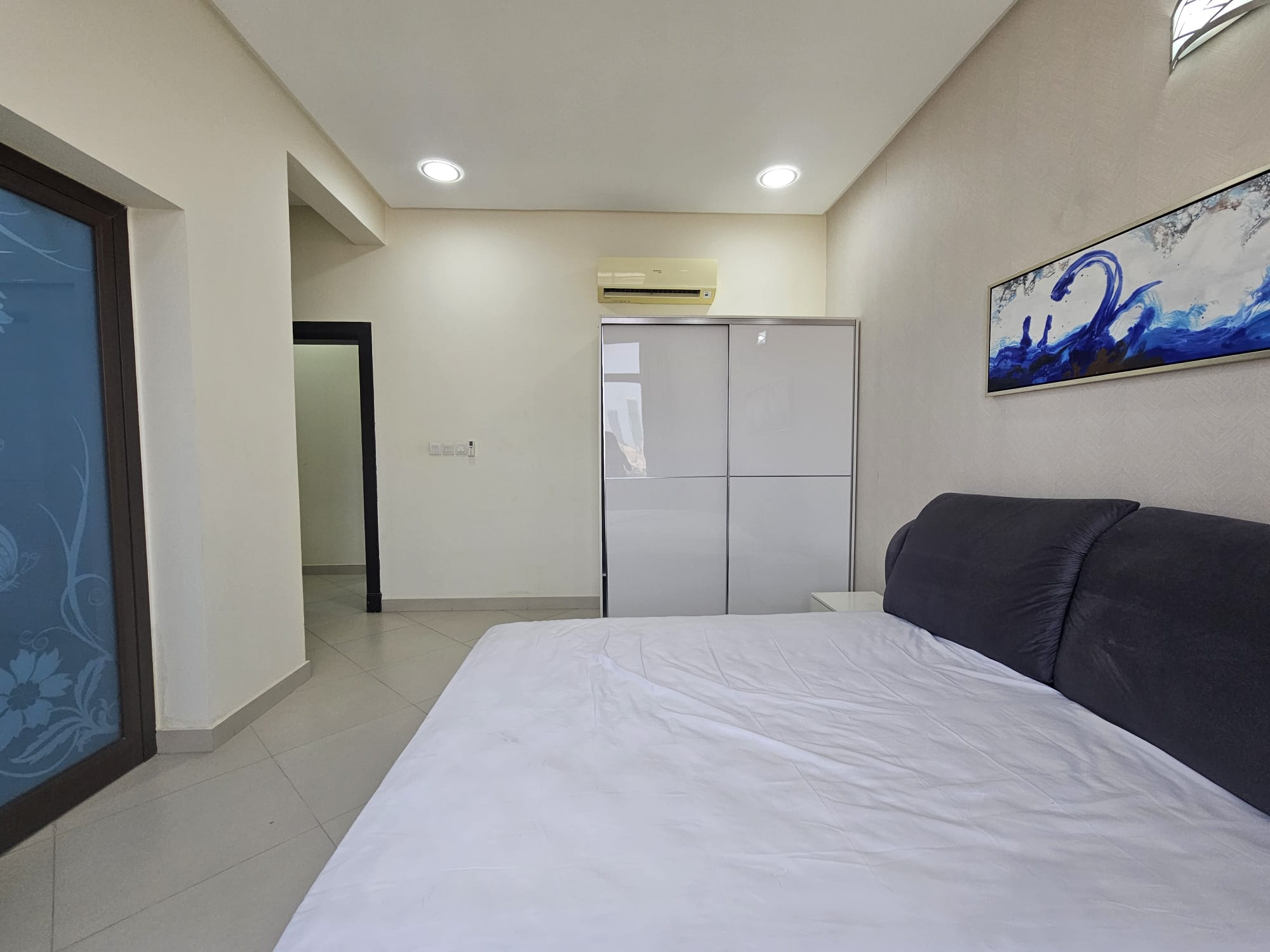 A bright, modern 2BR furnished flat bedroom with a large bed, minimalistic decor, and abstract art on the walls.