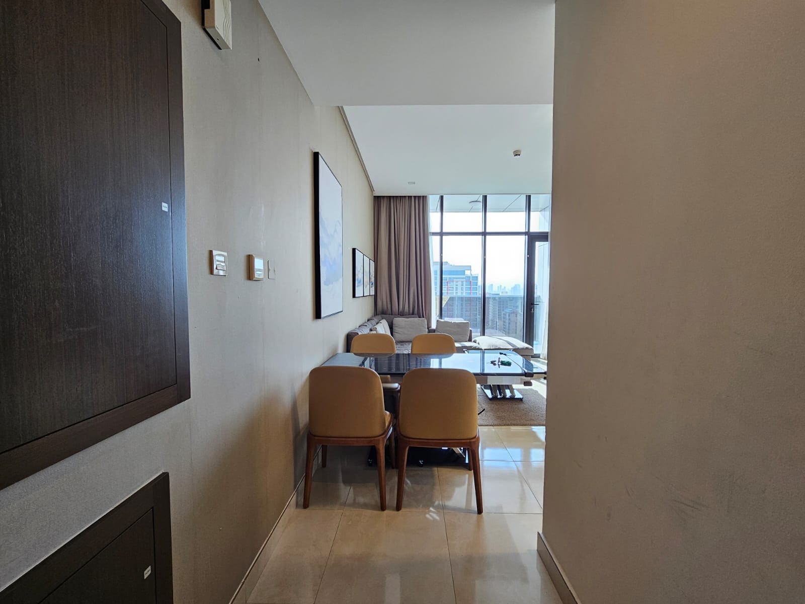 Modern apartment interior with a dining area leading to a living room with large Auto Draft windows overlooking the city.