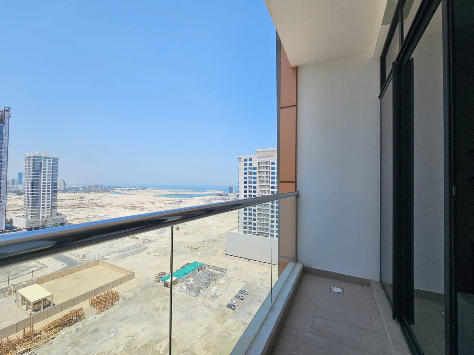 View from a high-rise balcony showing partial cityscape and coastline, with clear skies and surrounding buildings under construction.