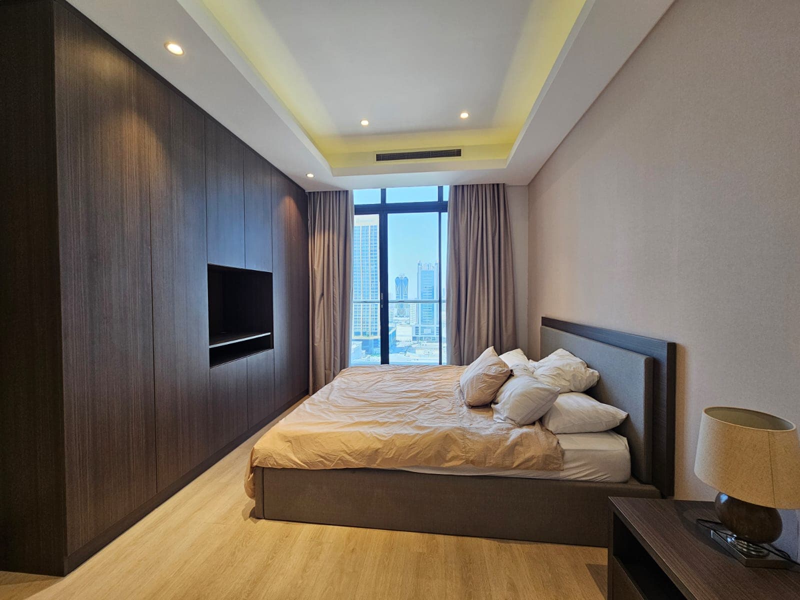 Modern bedroom with a large bed, wooden headboard, mounted tv, and a city view through the window.