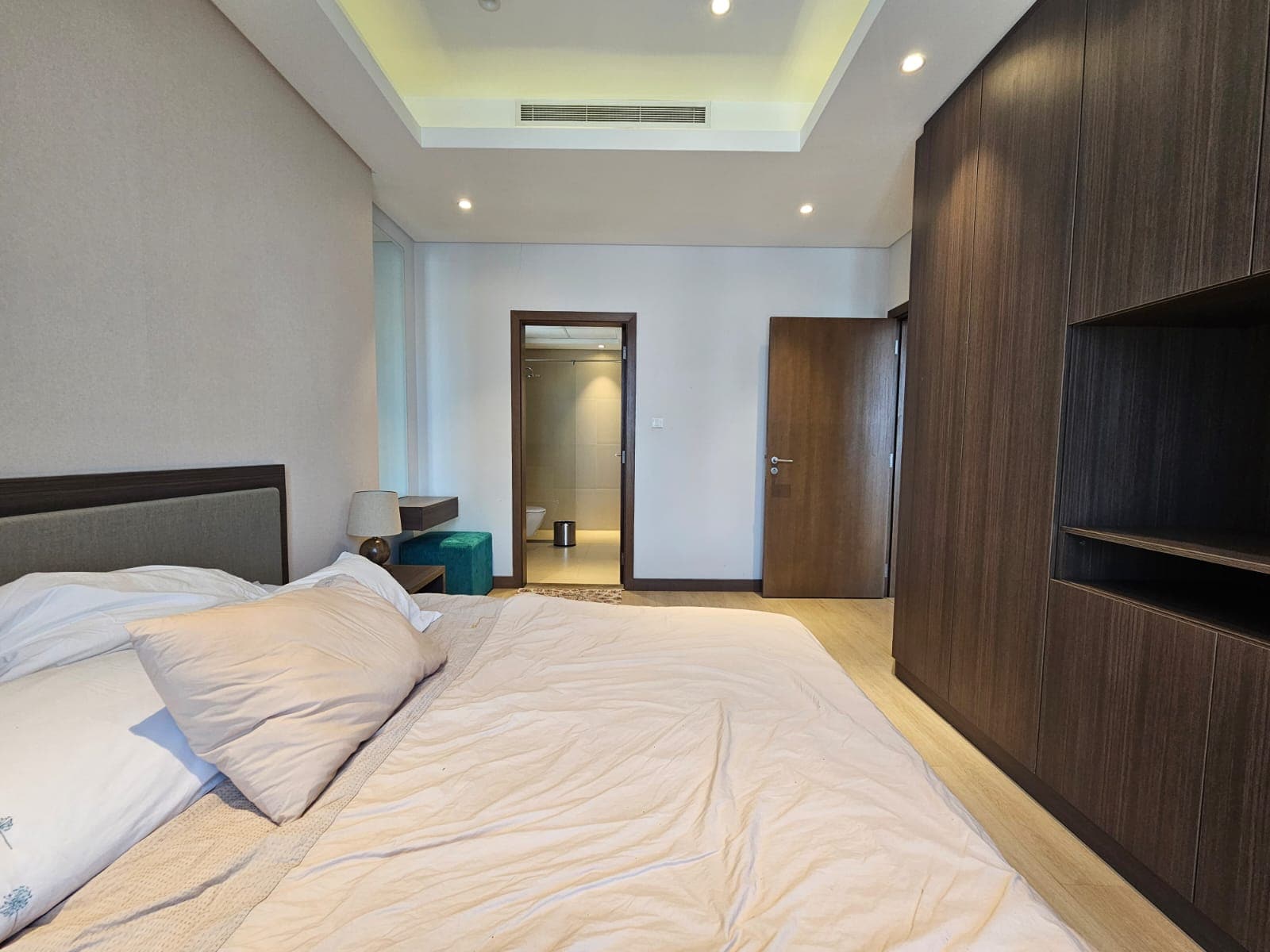 Modern bedroom interior with a large bed, wooden furniture, and recessed ceiling lighting. a doorway leads to another room.