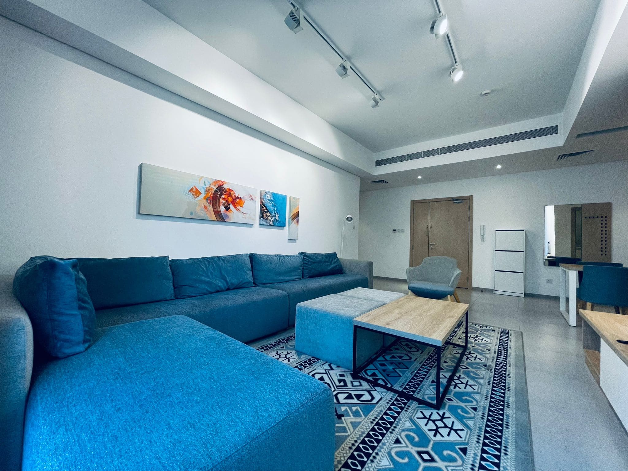 Modern living room with a blue sectional sofa, a geometric rug, and an auto draft colorful wall art piece.