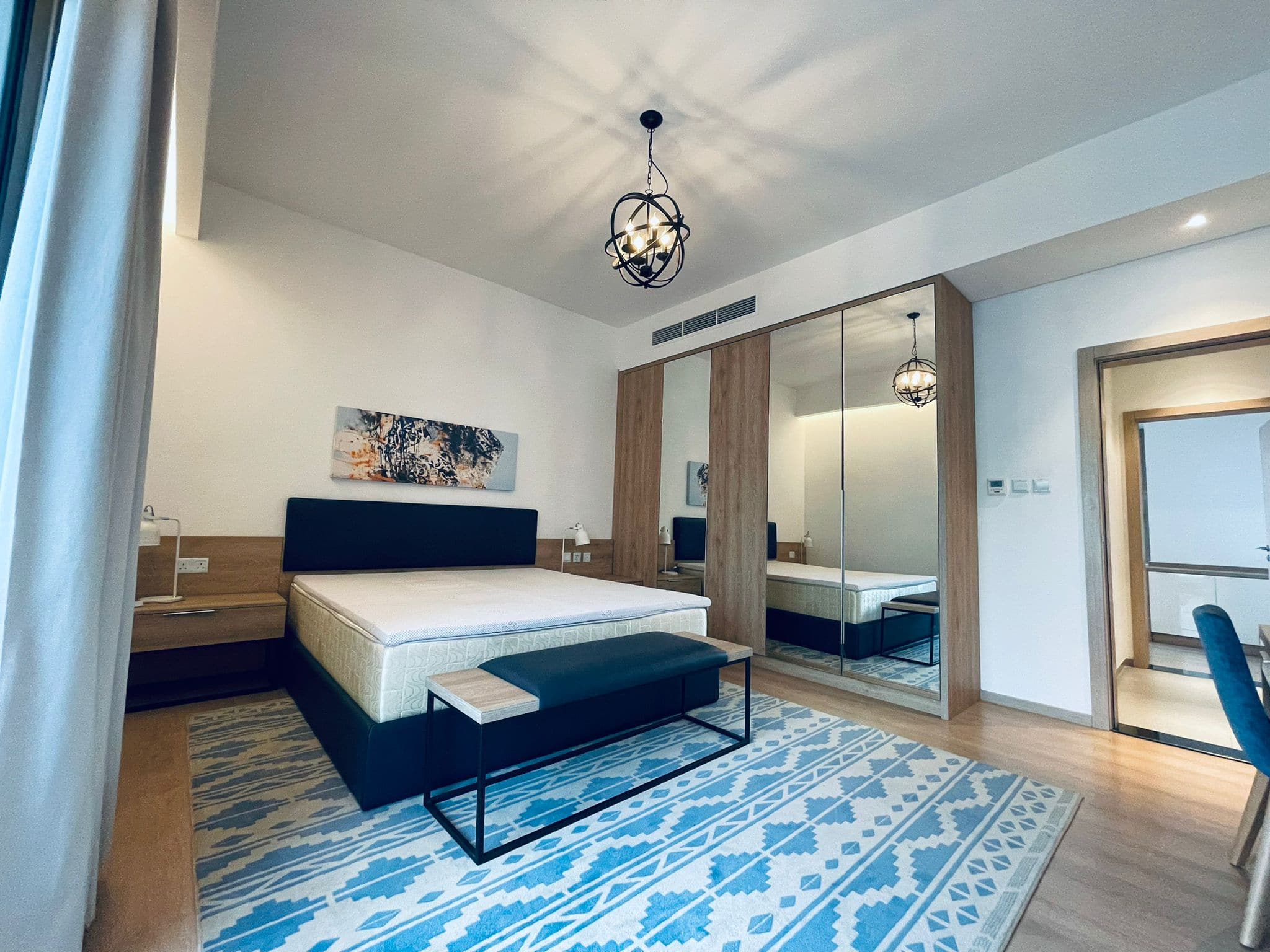 Modern bedroom with a patterned blue rug, wooden furniture, auto draft, and abstract wall art.