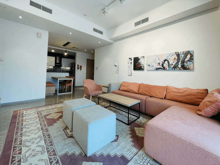 Luxury 1 BR apartment living room interior with l-shaped sofa, abstract wall art, and open-plan kitchen.