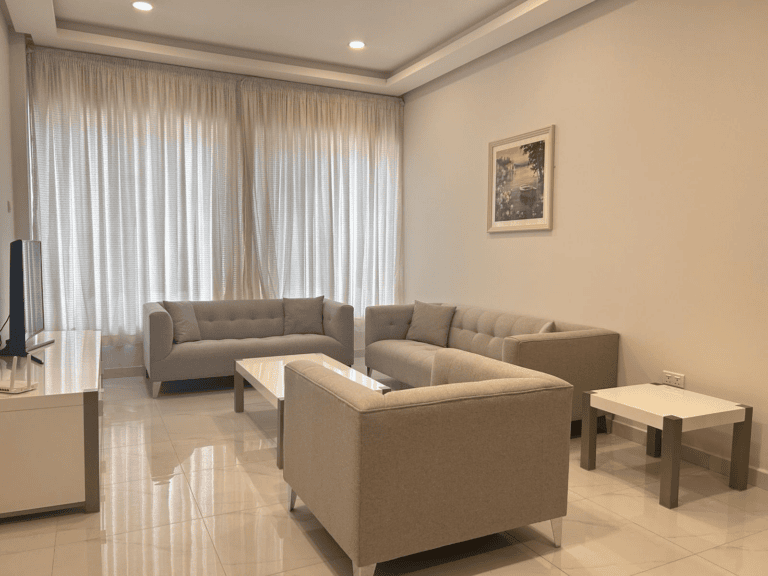 A modern living room in a luxury apartment, with beige sofas, a white coffee table, and a painting on the wall.