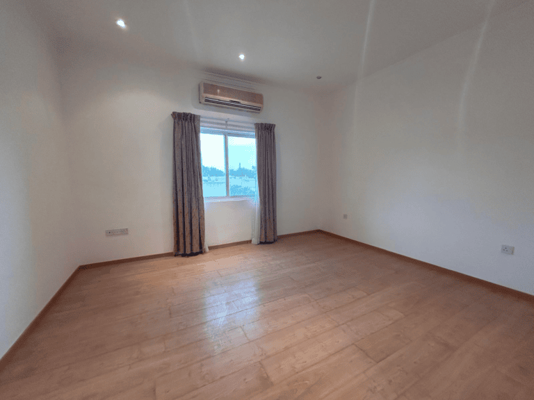 Empty room for rent with wooden flooring, white walls, an air conditioner, and curtains framing a window overlooking a scenic view.