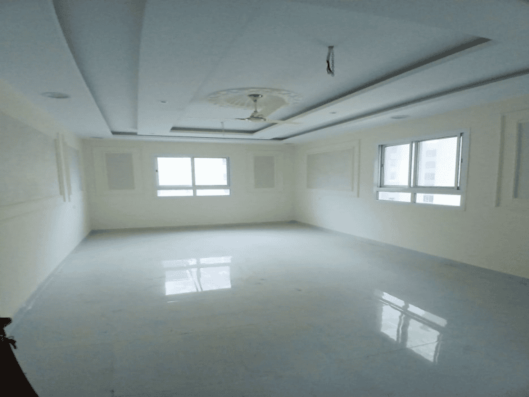 Empty white room with glossy tiled floor, large windows, and a recessed ceiling with a fan fixture in an apartment for sale.