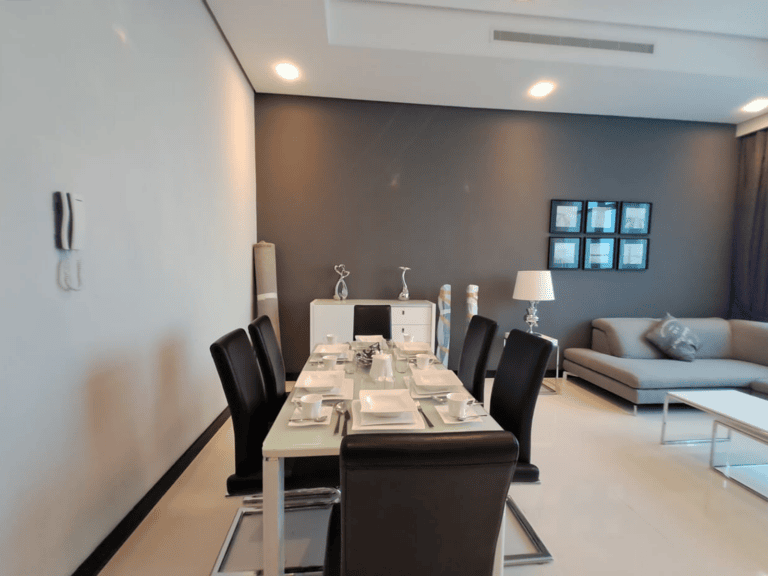 Modern dining room with a set table for six, sleek black chairs, and a gray sofa in the background, under ambient lighting in a fully-furnished 2 bedroom apartment.