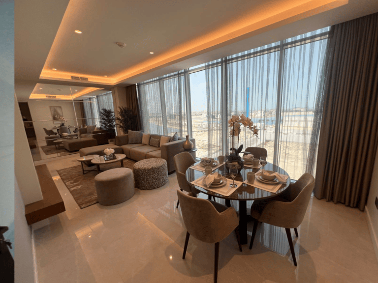Luxurious apartment dining and living area on Dilmunia Island with modern furniture, large windows offering a seaside view, and elegant interior decor.
