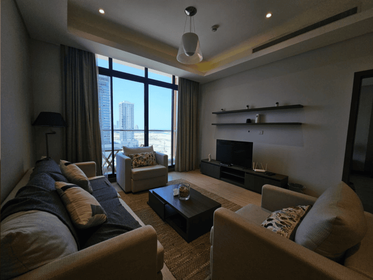 Modern flat with a living room featuring sofas, a coffee table, and a TV stand, complemented by large windows displaying city views and natural light.